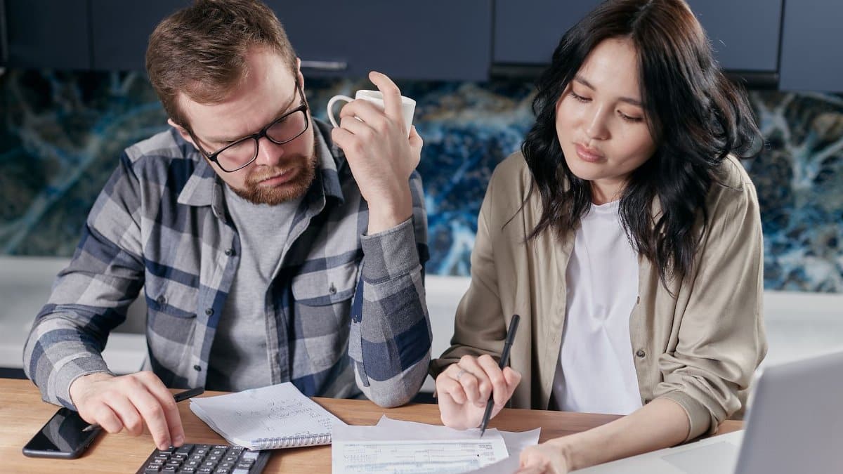A couple reviewing household bills and budget using a calculator and laptop at their kitchen table.