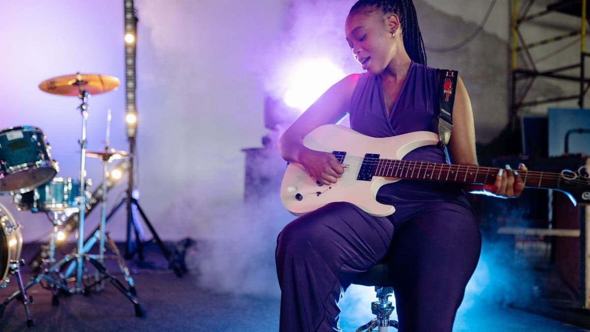 A woman passionately playing guitar on stage with vibrant lighting effects, creating an energetic atmosphere.