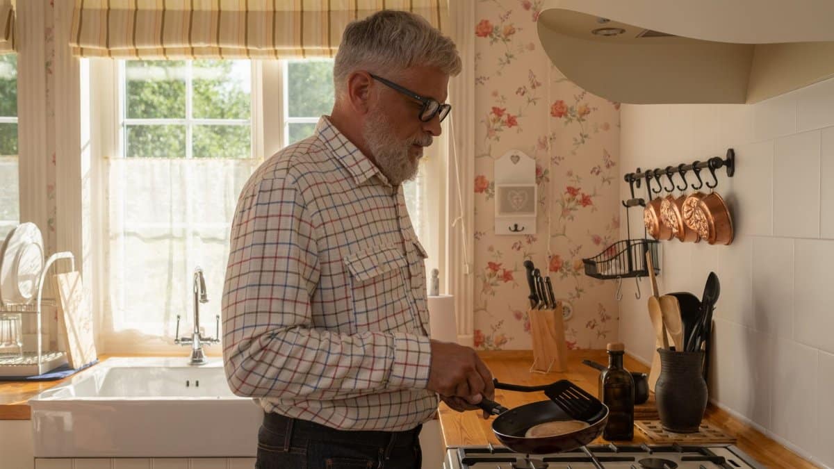Senior man cooking pancakes in a warm, sunny kitchen setting.