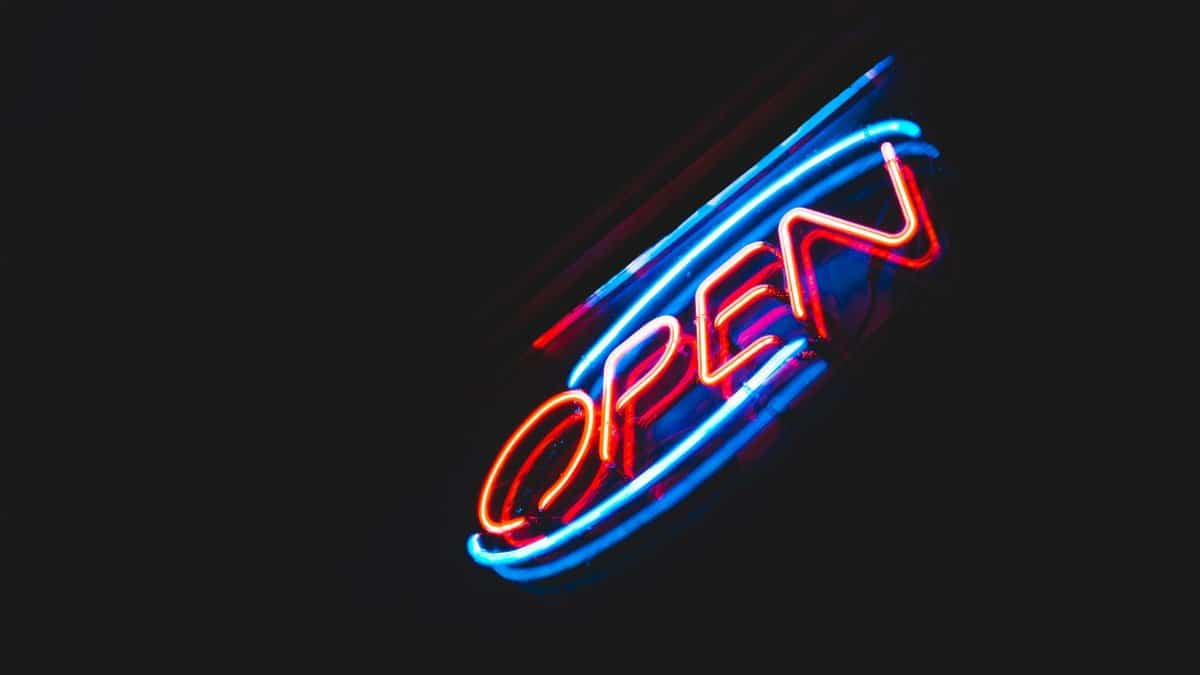 From below of Open sign with colorful neon lights hanging on building against dark night sky