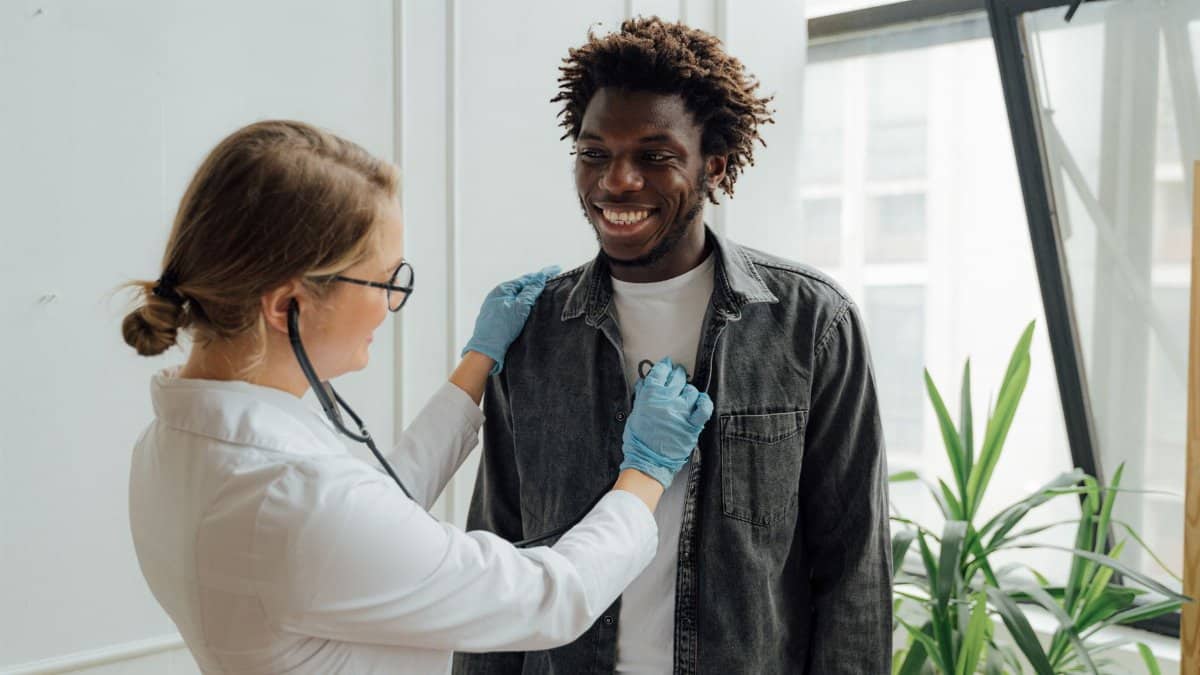 Doctor with stethoscope examining a smiling patient indoors, promoting health and care.