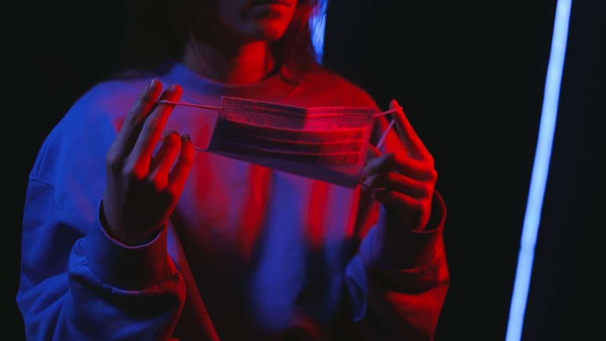 A person holds a face mask under dramatic red light, evoking themes of health and surrealism.
