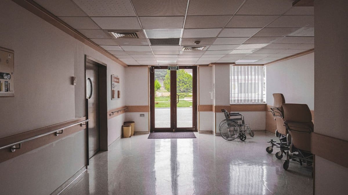 Hospital corridor with wheelchair, reflecting glass doors, and outdoor view. Ideal for healthcare themes.