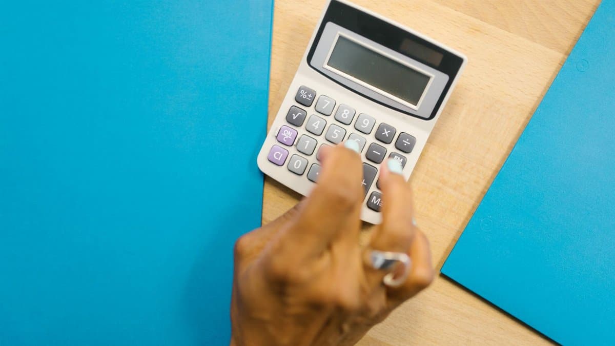 A hand using a calculator on a wooden desk surrounded by blue folders.