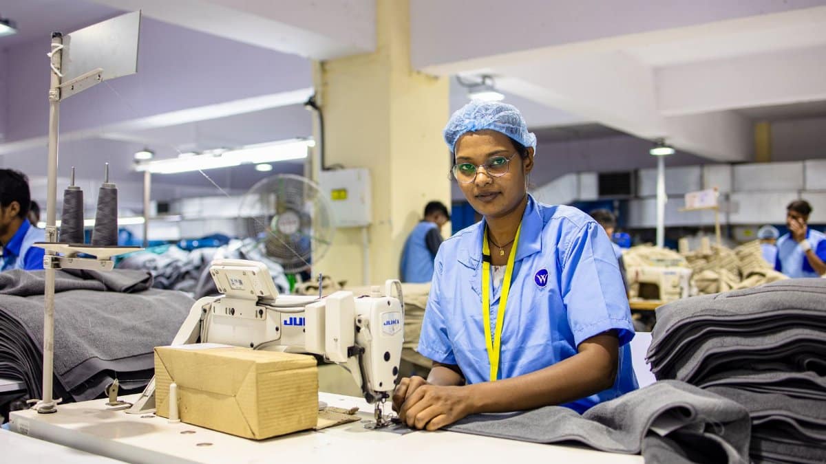 Female textile worker sewing fabric in an Indian factory setting.
