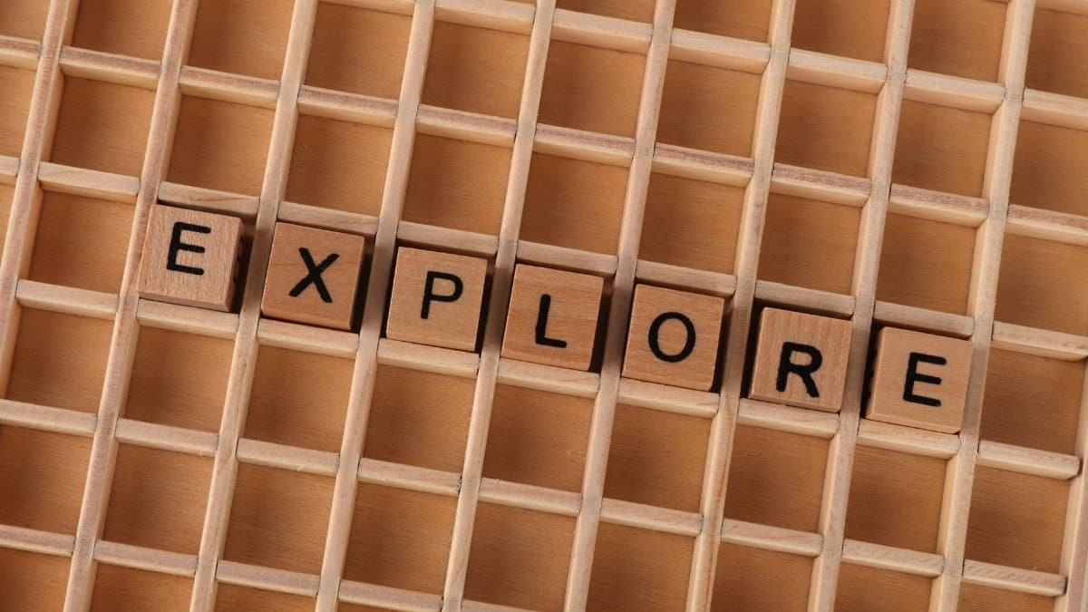 Wooden blocks spelling the word 'explore' on a wooden grid backdrop.