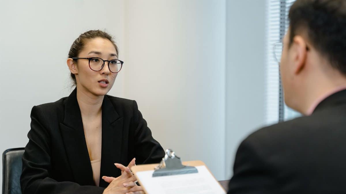 A focused interview scene in an office environment with business attire and a clipboard.