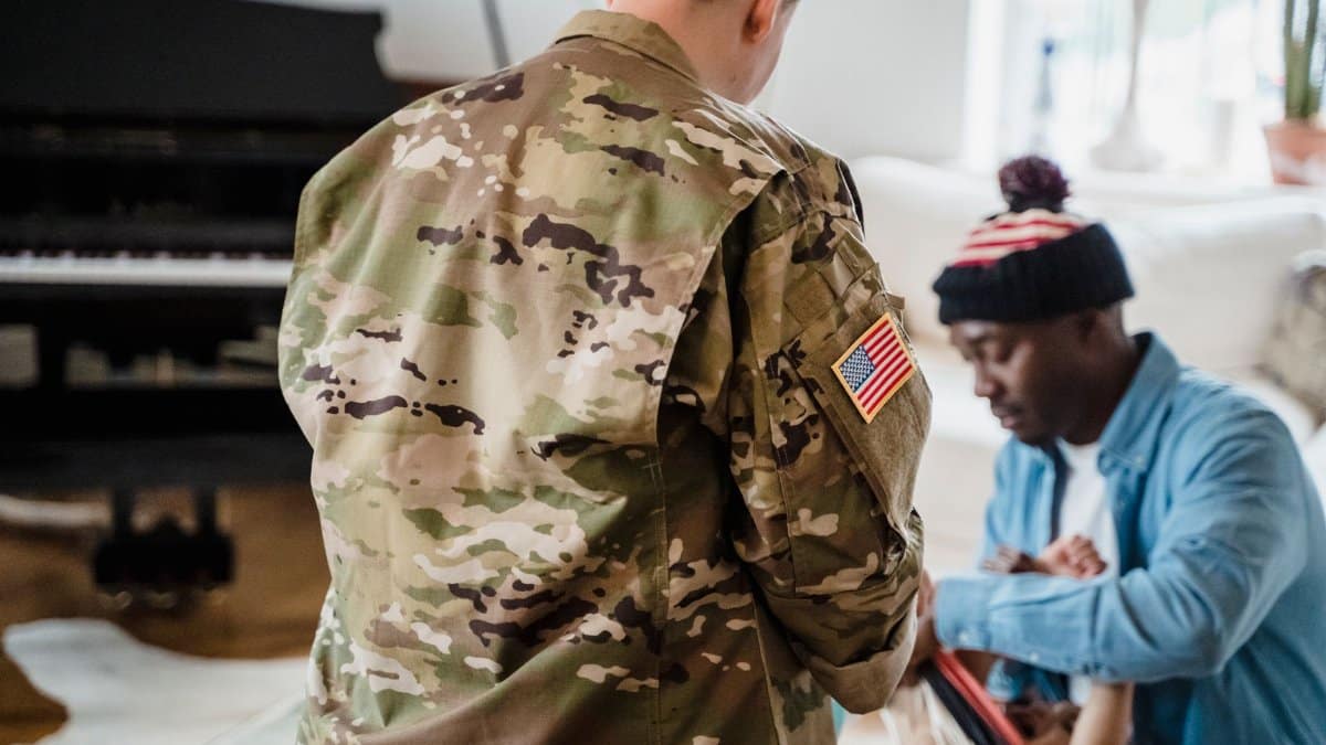 A soldier in camouflage uniform interacts with family at home, evoking themes of service and togetherness.