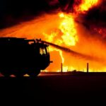 Dramatic image of a fire truck silhouette against a massive blaze, showcasing emergency response.