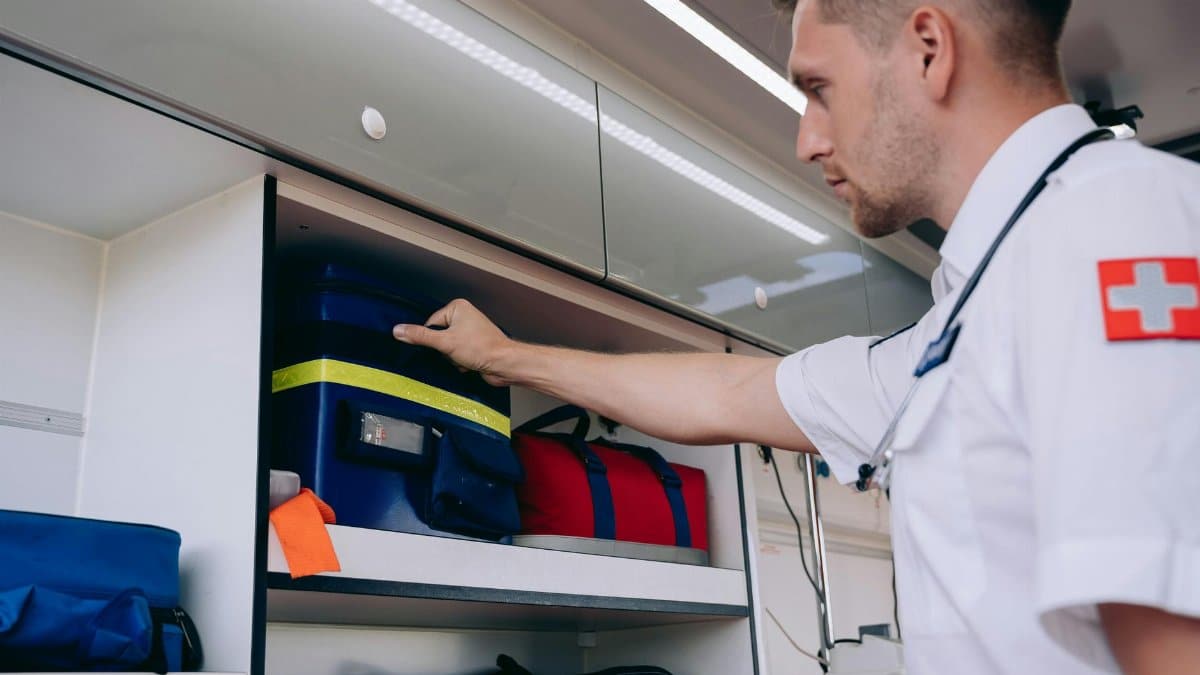 A paramedic organizes medical supplies inside an ambulance shelf for emergency preparedness.