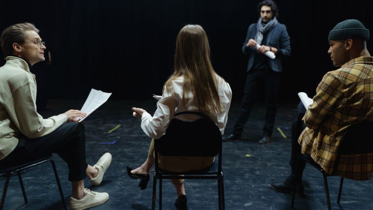Group of actors in rehearsal with director, practicing for a theater performance.
