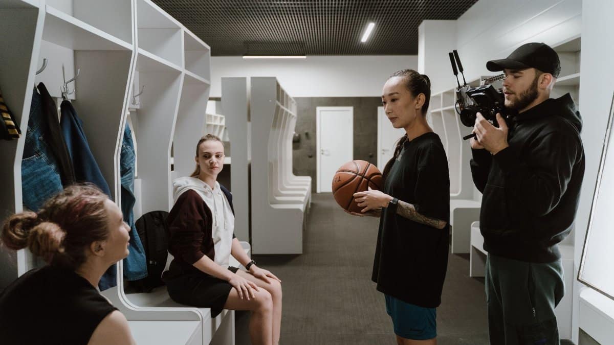 A candid behind-the-scenes look inside a basketball locker room during an interview with athletes and a cameraman.