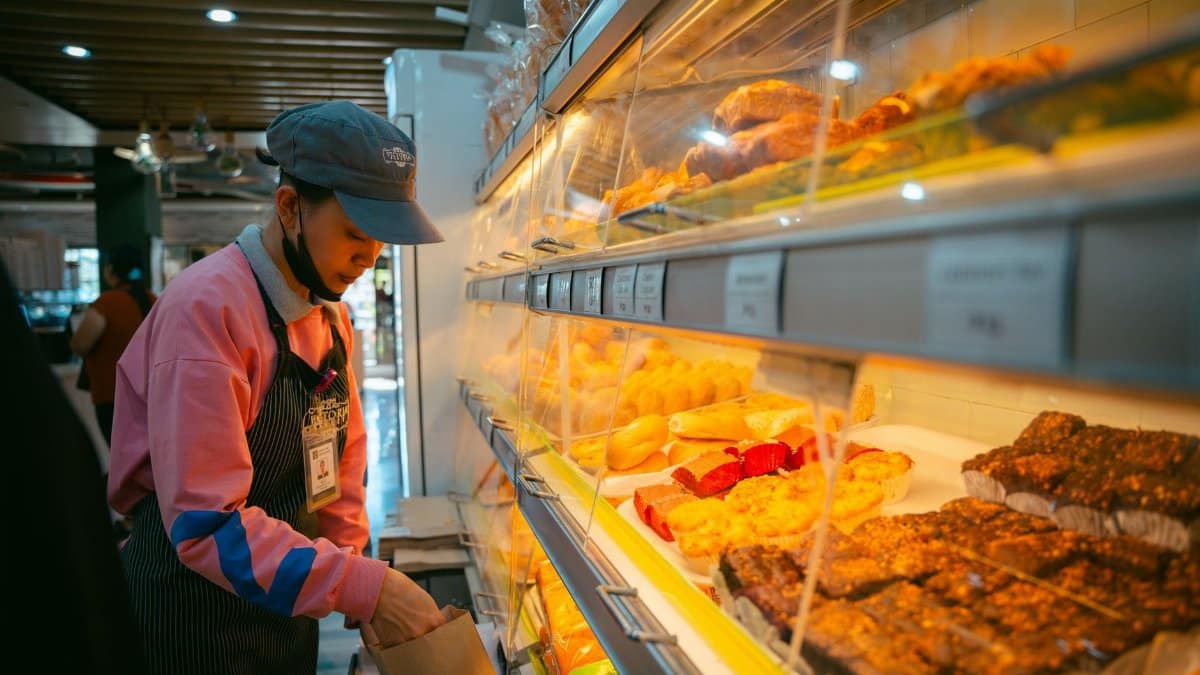 A bakery employee wears an apron and organizes pastries in a well-lit Baguio store.
