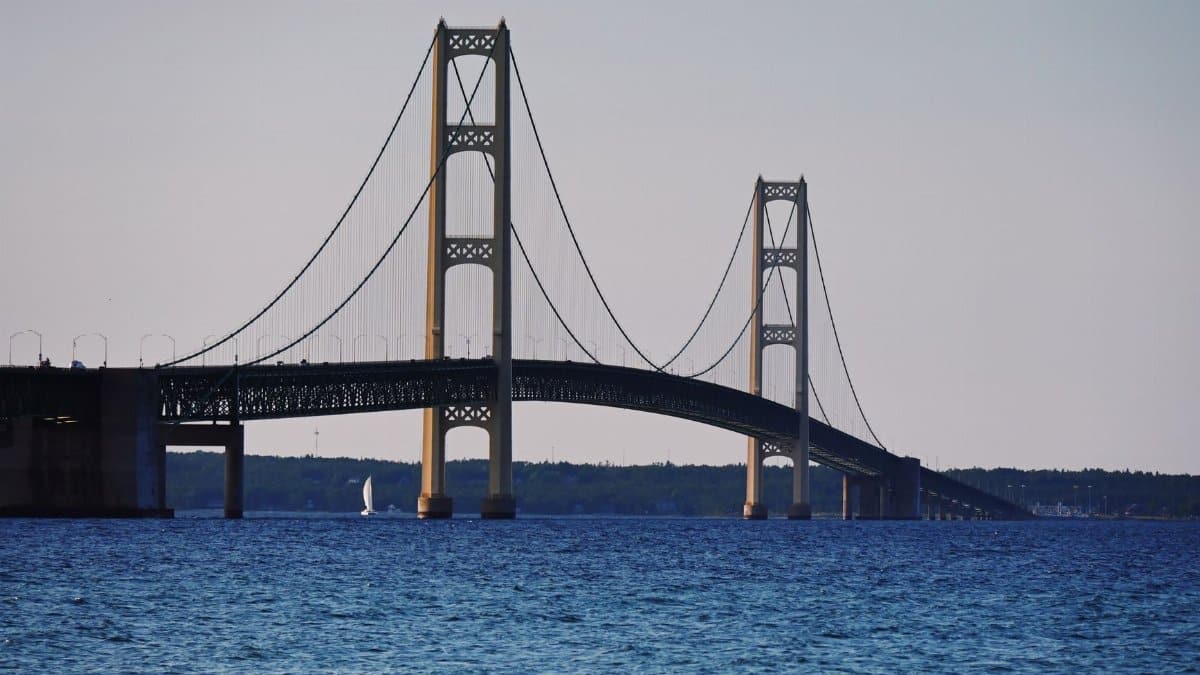 Serene view of Mackinac Bridge spanning the straits with a sailboat passing underneath.