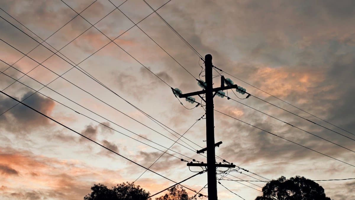 Silhouette of utility poles and cables against a vivid evening sky, highlighting urban infrastructure.