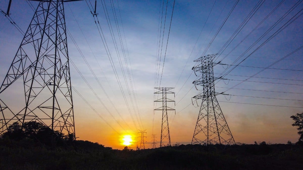 Silhouetted power lines and towers against a striking sunset sky, illustrating energy supply themes.