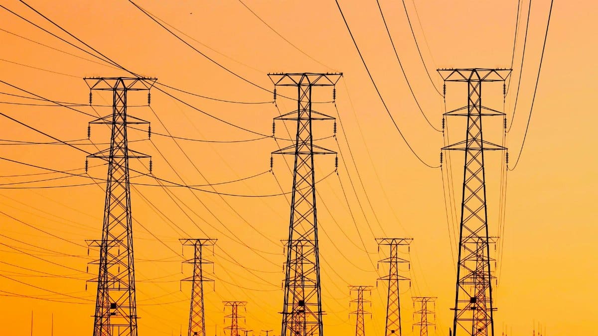 Silhouetted power lines against a vibrant orange sunset, symbolizing energy and infrastructure.
