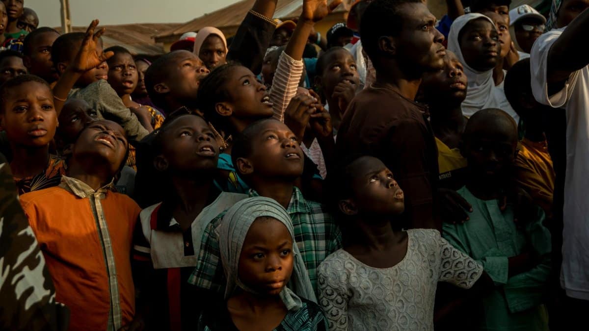 A diverse crowd of African children and adults looking upwards during a community gathering in Cape Town, South Africa.