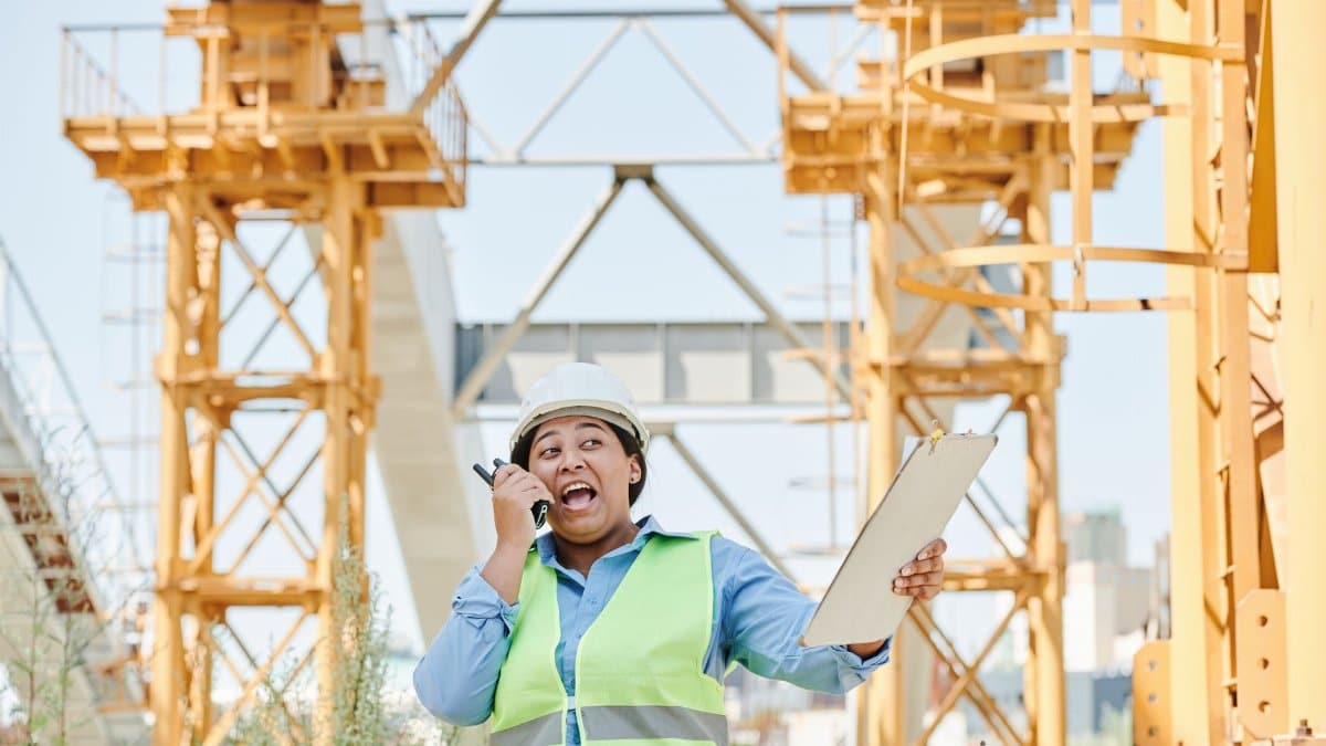 Female engineer using walkie-talkie while holding clipboard on a construction site.