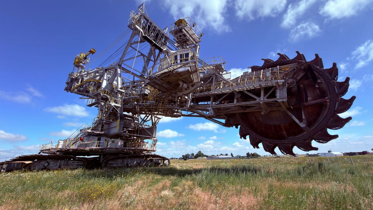 A large bucket wheel excavator under a clear blue sky in an open field.