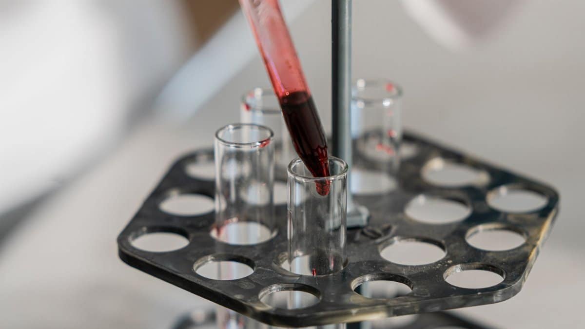 Red liquid being transferred into test tubes in a lab setting for research.