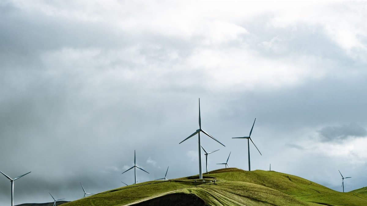 Wind turbines on lush hills with a dramatic cloudy sky, symbolizing clean energy and sustainability.