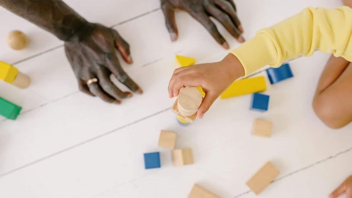 A parent and child playing together with wooden blocks on a white floor, fostering connection.