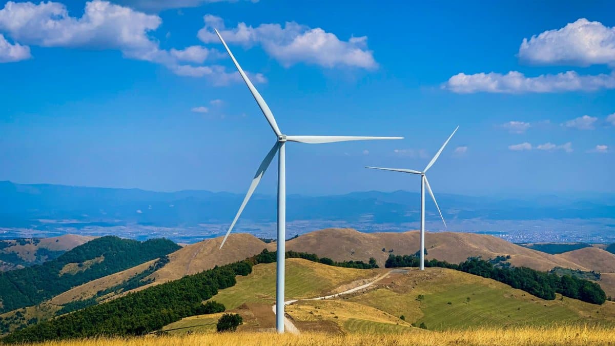 Scenic view of wind turbines on green hills under a clear blue sky, symbolizing renewable energy.
