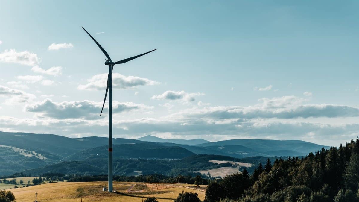 Picturesque view of a wind turbine against rolling hills and blue sky, symbolizing renewable energy.