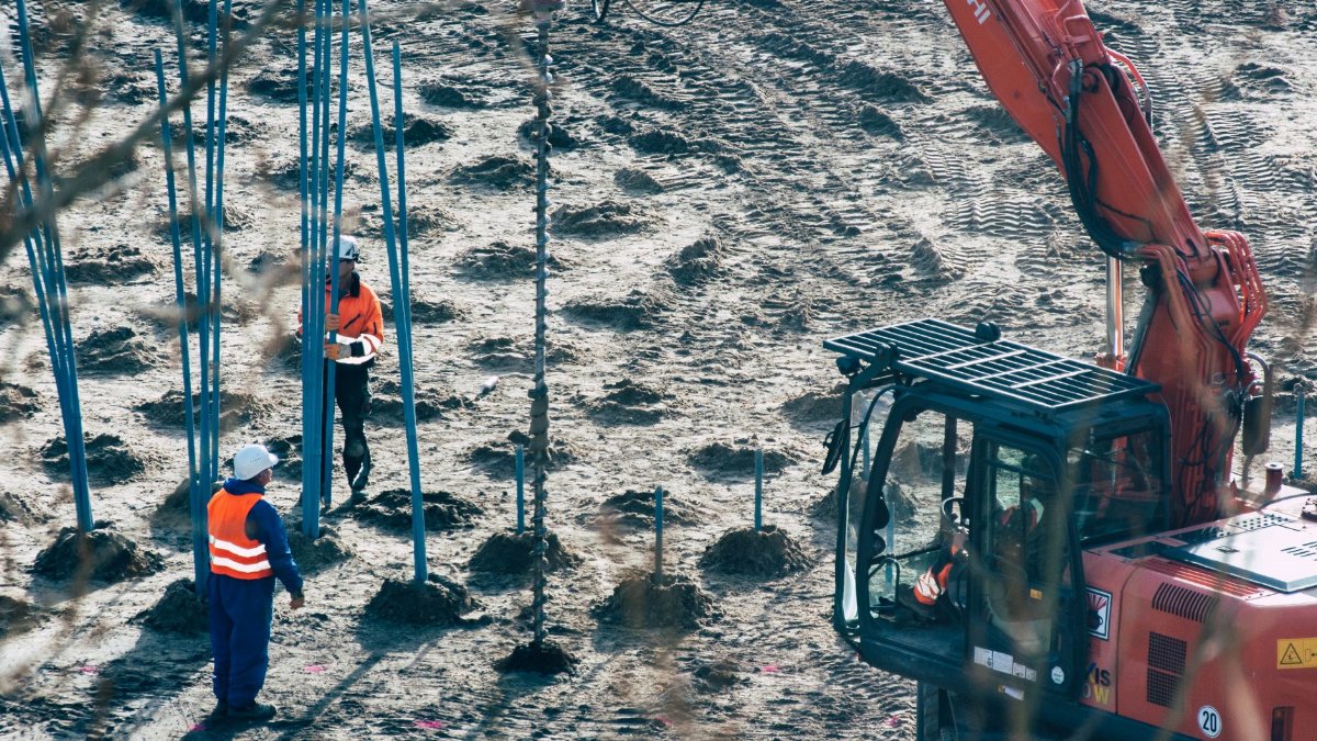 A construction site with workers and an excavator drilling holes in the ground.