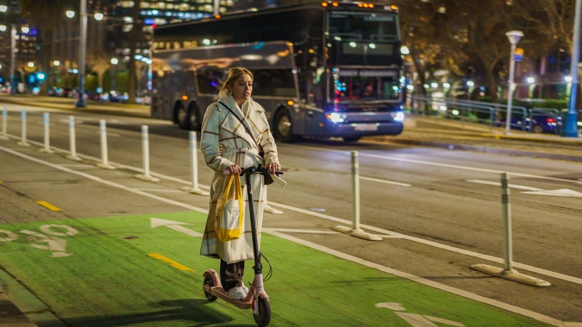 Young woman rides electric scooter in city at night with traffic.