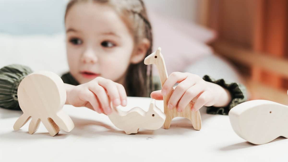 A young girl engaging in imaginative play with wooden animal toys in a bright indoor setting.