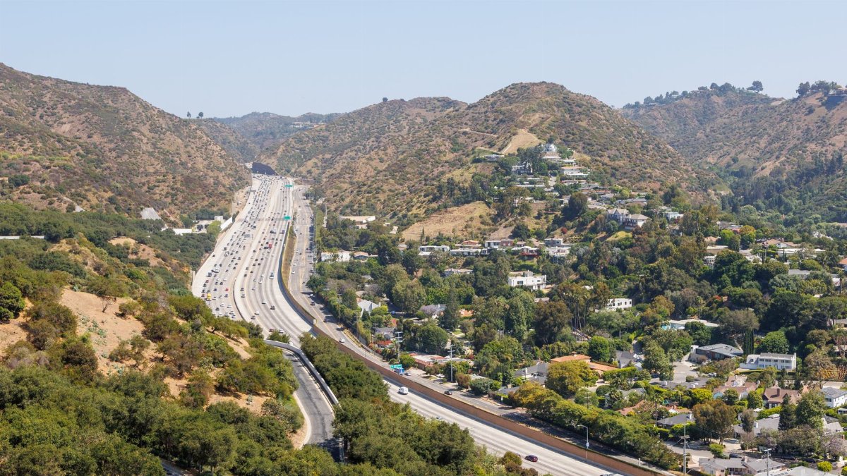 Aerial view of a busy Los Angeles freeway winding through picturesque hills and lush greenery.