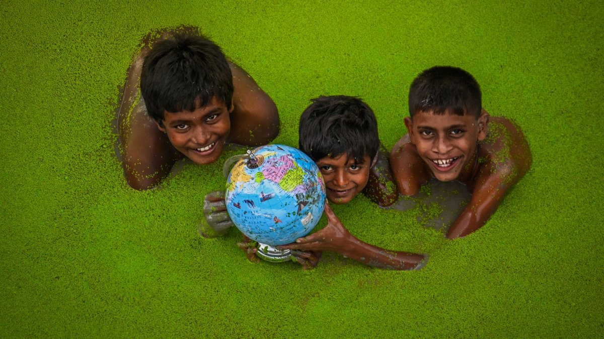 Three children play happily in a green lake in India, holding a globe.