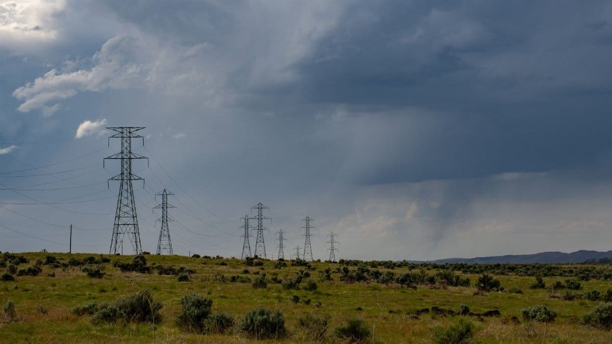 Transmission towers in a grassy field under a dramatic cloudy sky indicating incoming storm.