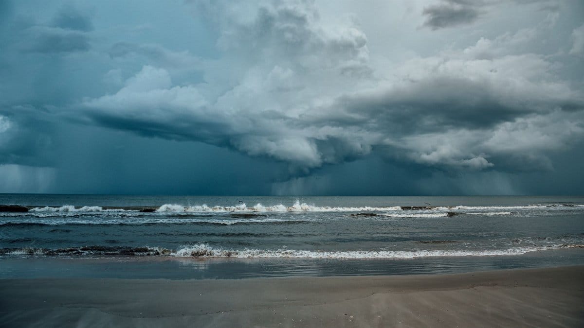 A striking image of storm clouds gathering over a calm ocean shoreline, creating a dramatic seascape.