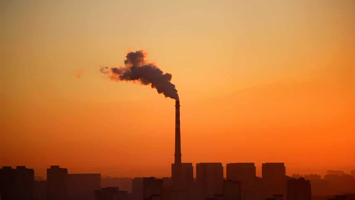 Industrial smokestack emitting smoke during sunset, highlighting environmental impact.