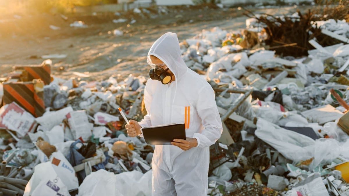Environmental scientist assessing pollution wearing protective gear at a landfill.