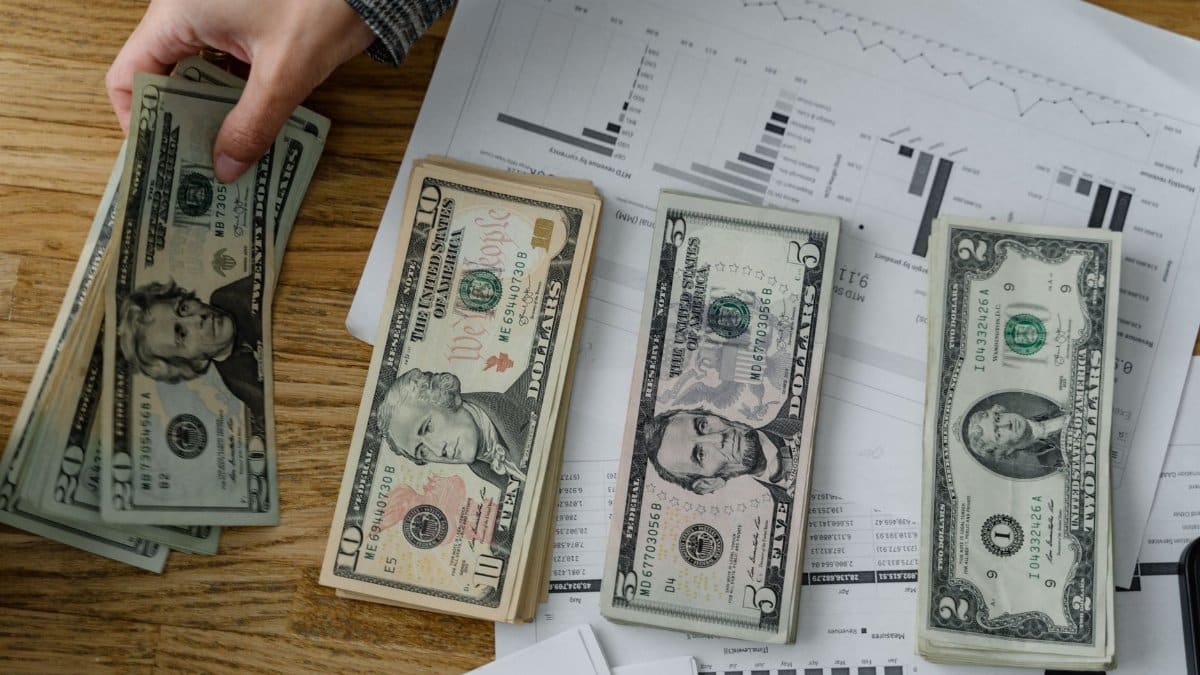 Person holds US dollars over financial papers, showing income or budget analysis.