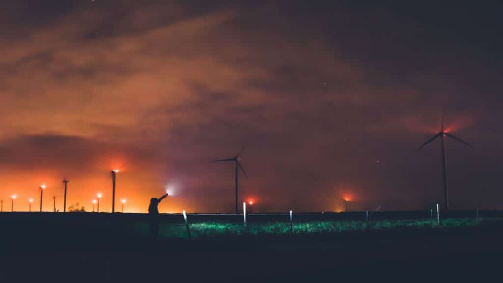 Silhouette of a person near wind turbines at night under cloudy sky in Texas.