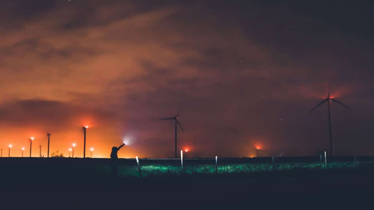 Silhouette of a person near wind turbines at night under cloudy sky in Texas.