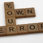 Scrabble tiles spelling 'Own Your Error' on a white background.