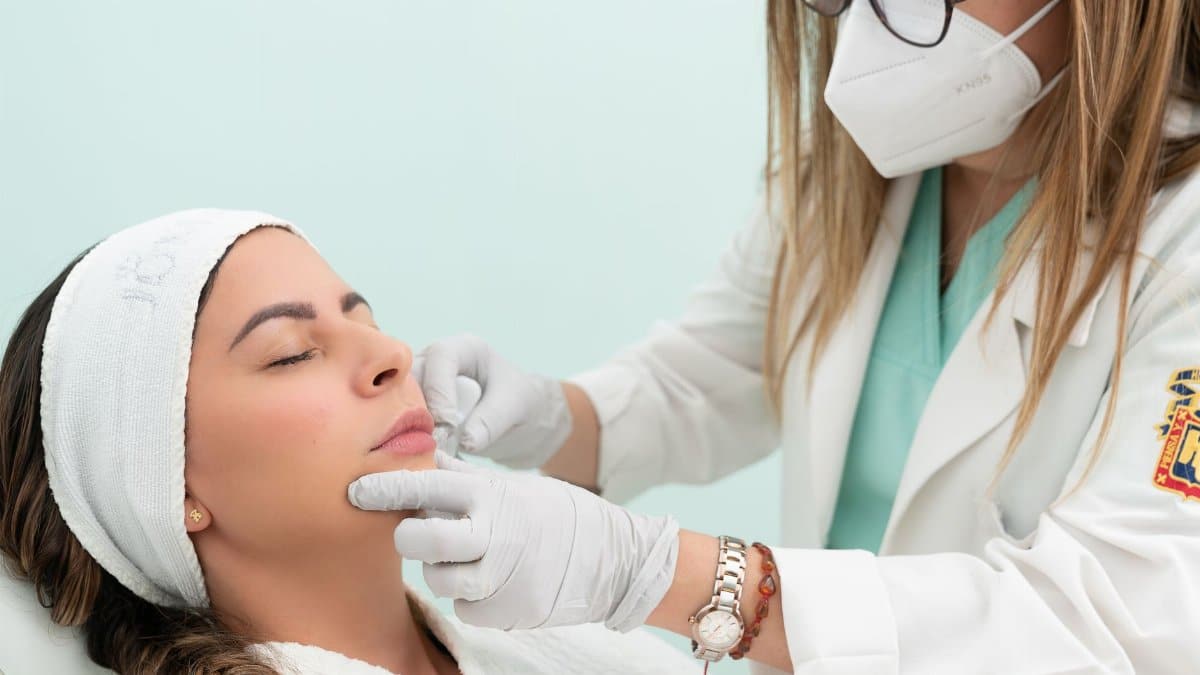 Doctor performing cosmetic treatment on a woman with eyes closed in a clinical setting.