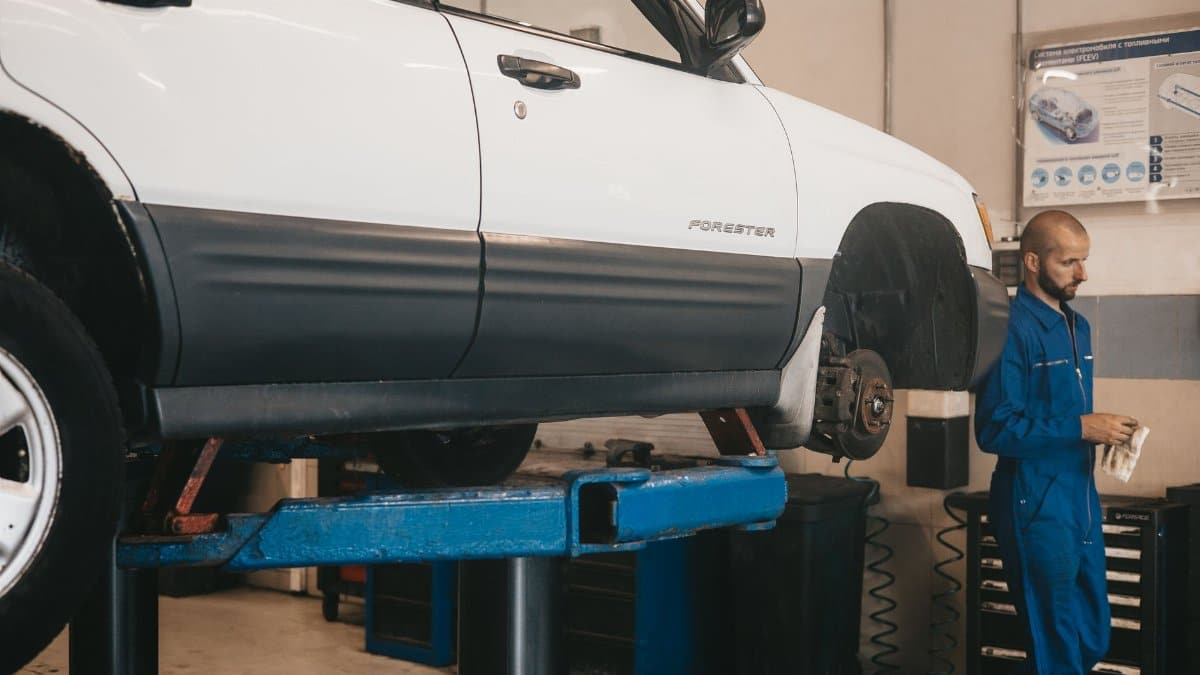 Mechanic evaluating a car on a lift for maintenance in an auto workshop.