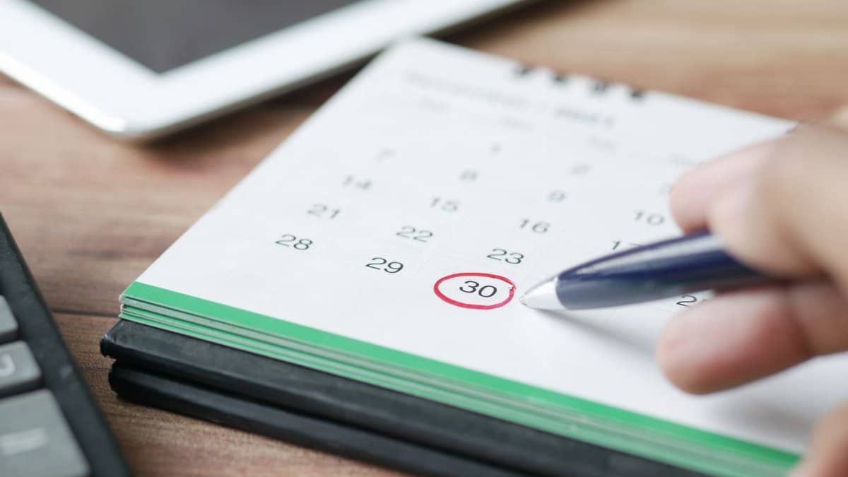 Close-up shot of a hand marking a date on a calendar with a pen, emphasizing planning and scheduling.