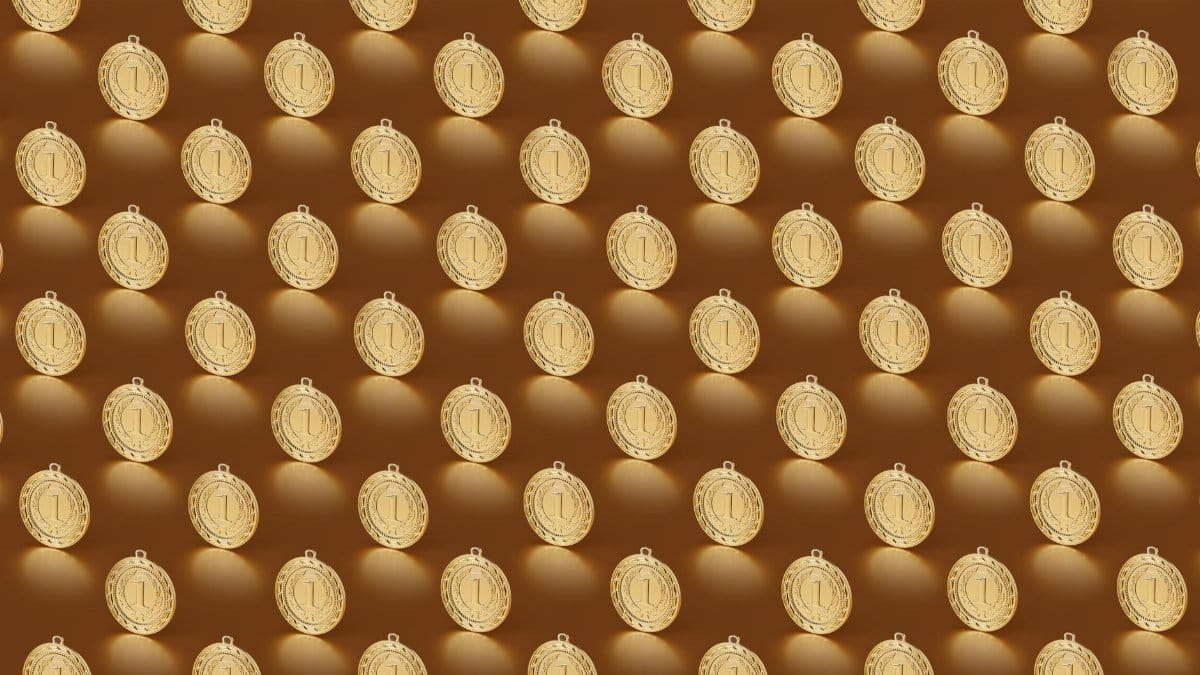 Multiple gold medals arranged in a repeating pattern on a brown backdrop.