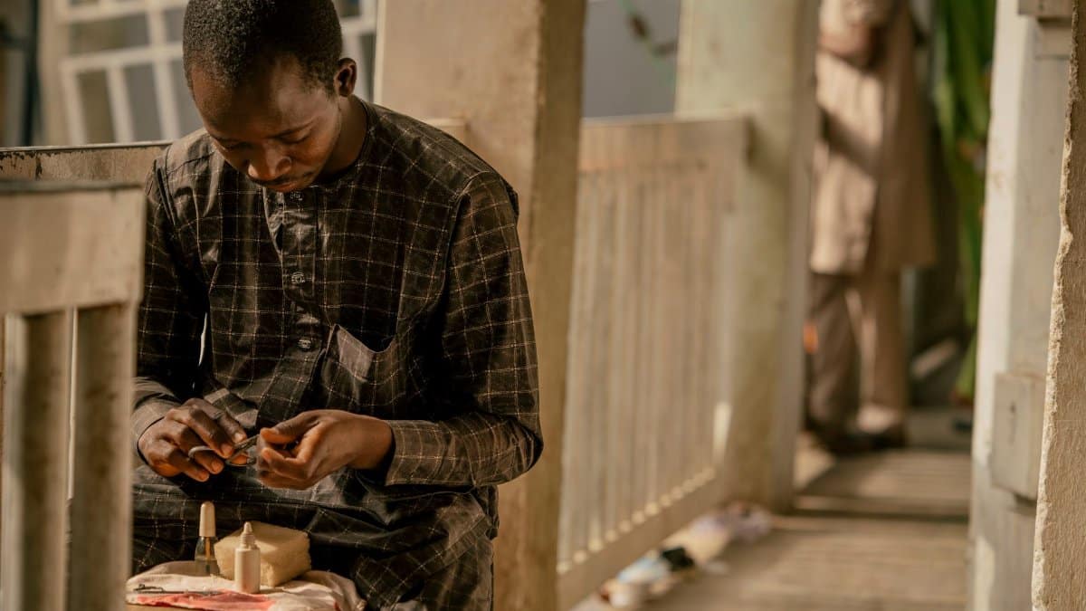 A young Nigerian artisan carefully crafting on a sunny balcony, showcasing traditional work.