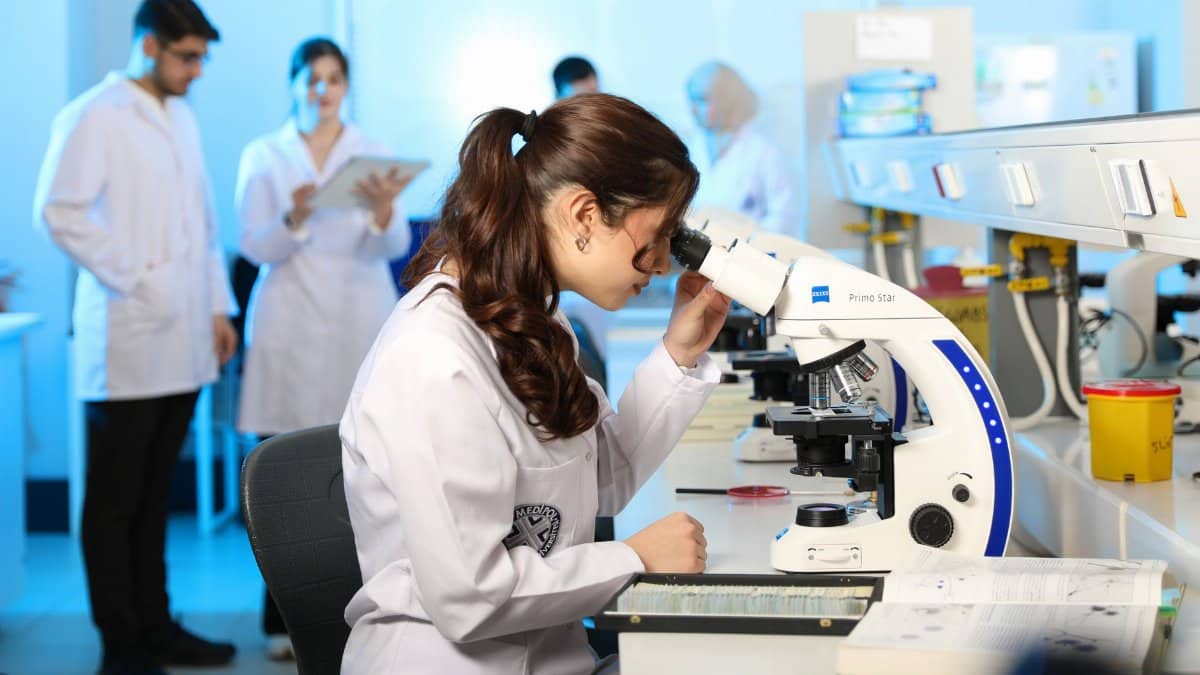 Young female scientist examining samples under a microscope in a modern laboratory setting.