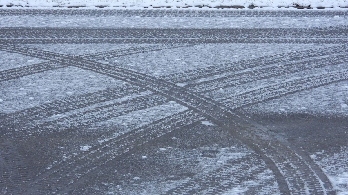 Snow-covered road with intersecting tire tracks and a dusting of snow, illustrating winter conditions.