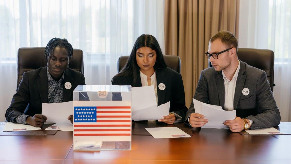 A diverse group of professionals examining papers near a voting box indoors.